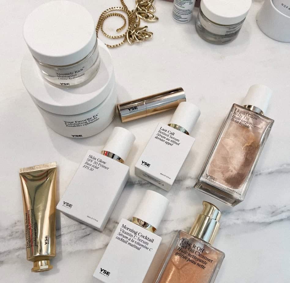 Skincare products and jewelry on a white marble surface, including creams and serums.