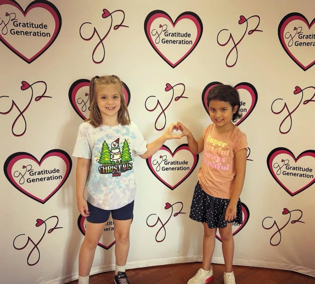 Gratitude Generation Summer Camp 2026 - two kids pose in front of a Gratitude Generation backdrop after a volunteering event.