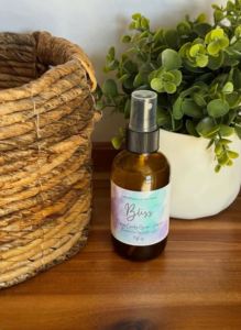 Aromatherapy spray bottle with green plant in a white pot on wooden surface.