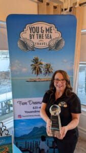 A woman holding an award at Ocean City Moms event with beach and palm trees in background.