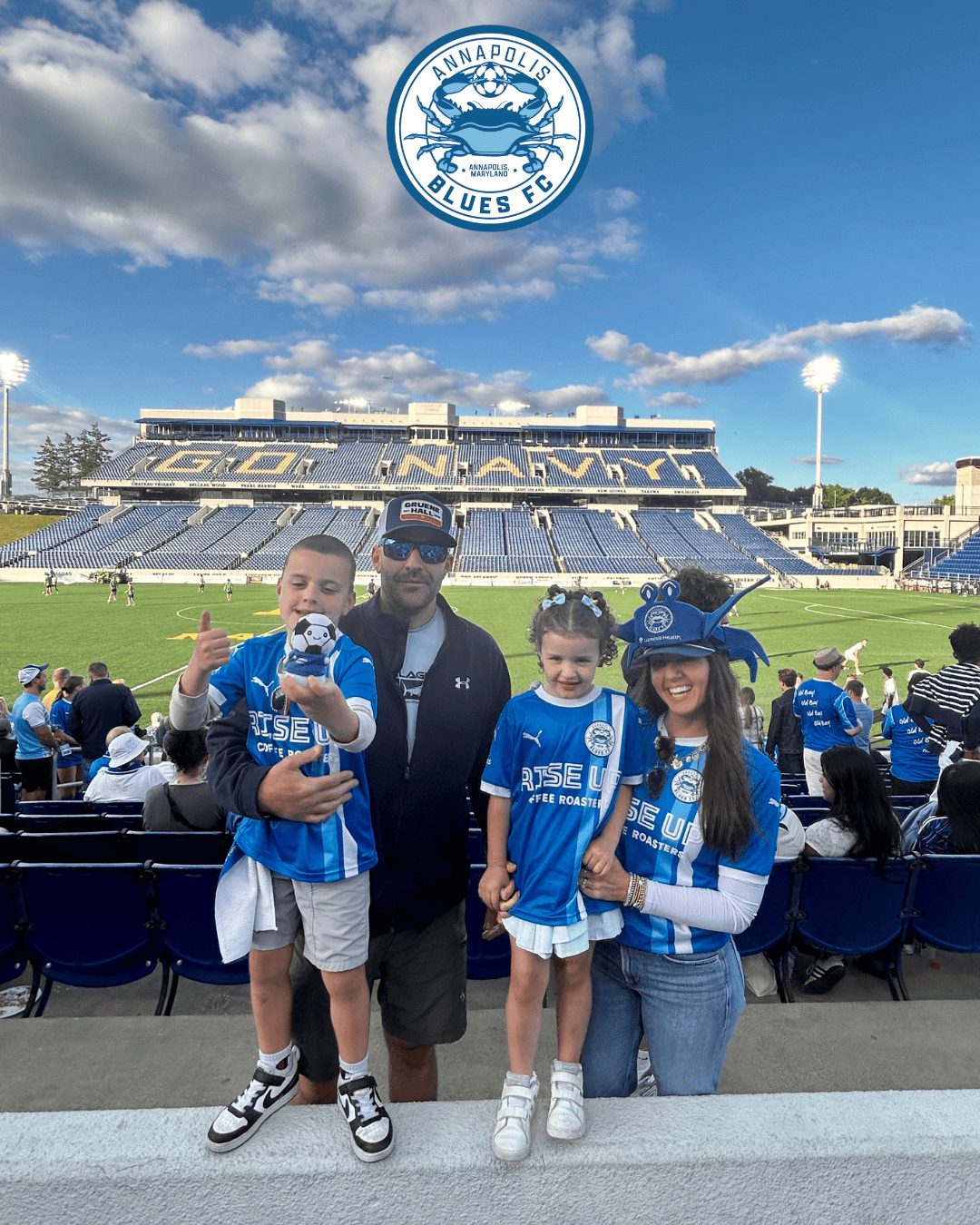 Ocean City Blues FC fans at a stadium with family, blue team jerseys, and a clear sky.