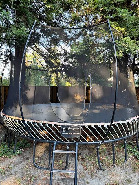 weathered backyard trampoline with a damaged safety enclosure