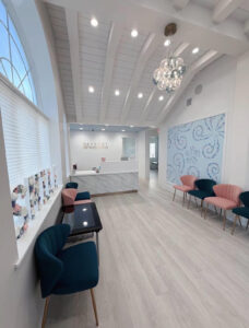 Modern dental office interior with pink and blue chairs, high ceiling, and decorative wall art.