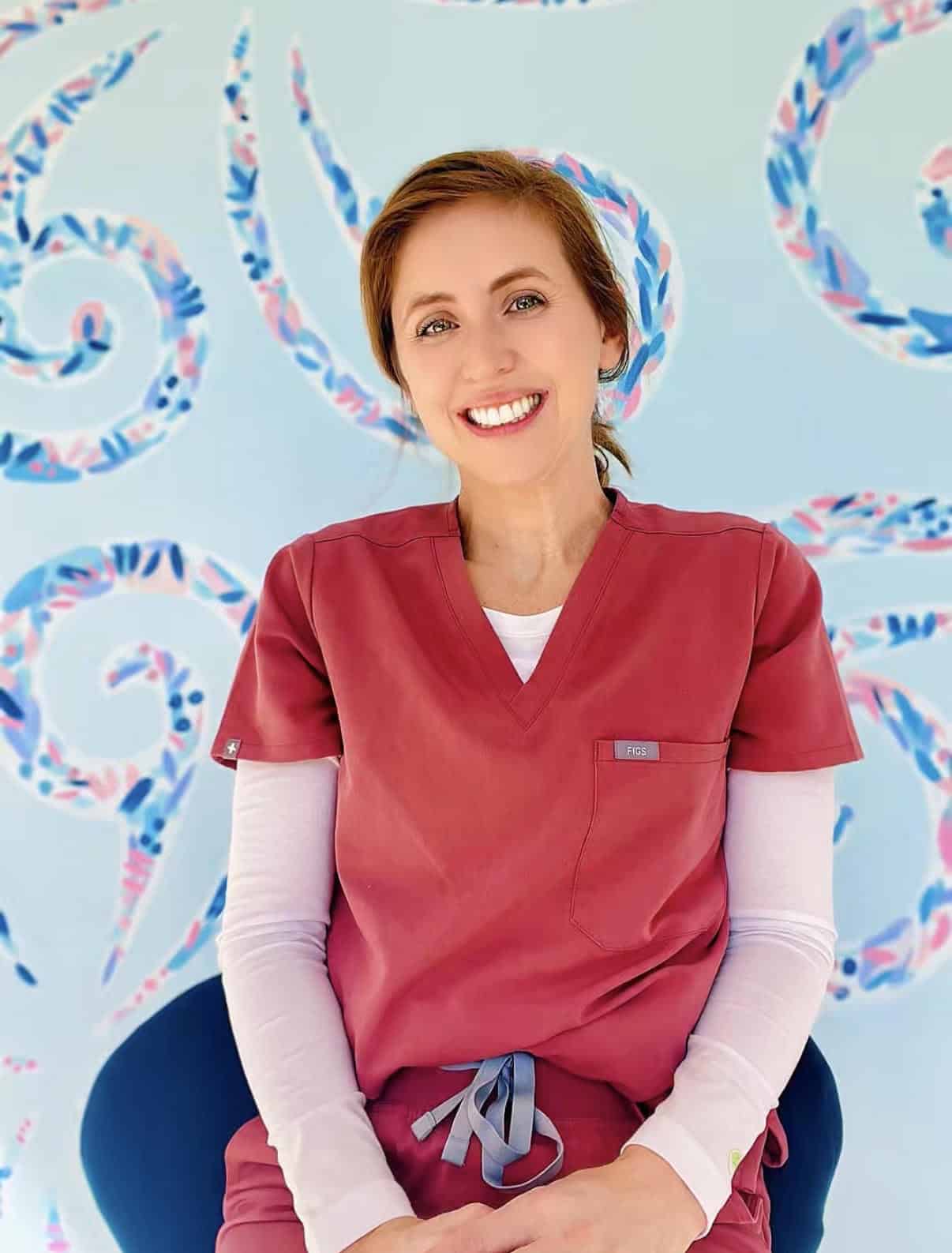 Smiling woman in red scrubs in front of colorful ocean-themed background.