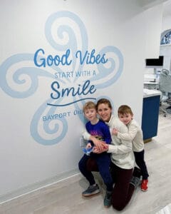 Happy children with a smiling woman at Bayport Orthodontics office wall with 'Good Vibes Start witha.