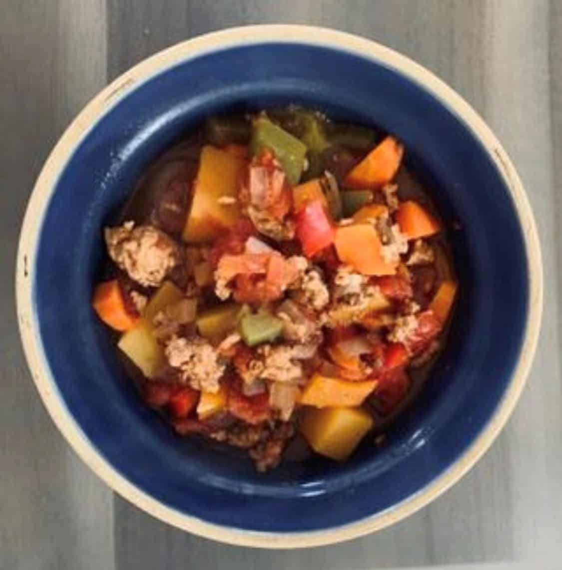 Colorful vegetable and ground meat stew in a blue bowl on a wooden table.