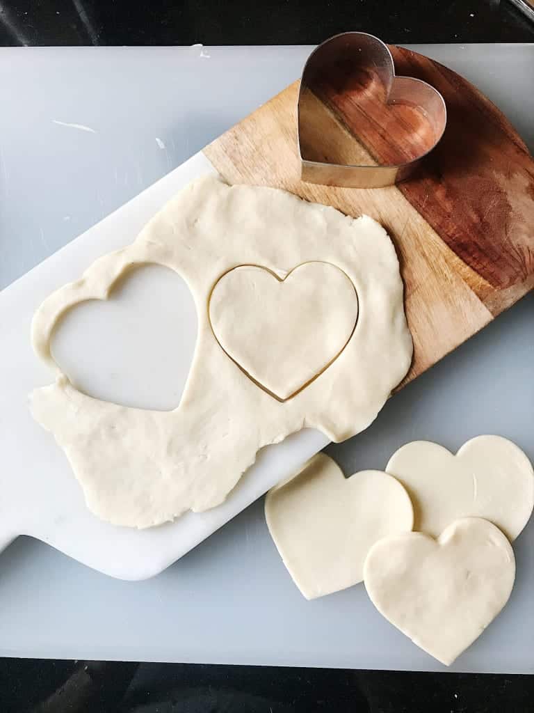 Heart-shaped cookies cut from dough on a baking sheet with cookie cutters.